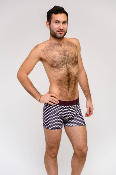 Portrait of a handsome male model with perfect body, standing naked in shorts, posing on a white background. Black hair. Close Studio Shot - Zdjęcie, obraz