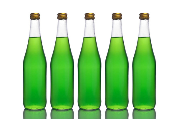 Cinco grandes botellas de vidrio con líquido verde se colocan sobre una superficie de espejo sobre un fondo blanco en el centro
. - Foto, Imagen
