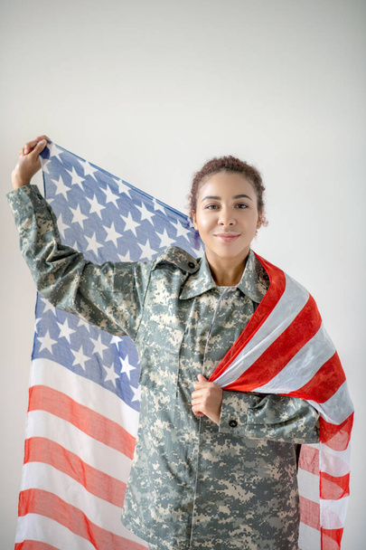 Patriotic young pretty servicewoman holding national flag - Foto, imagen