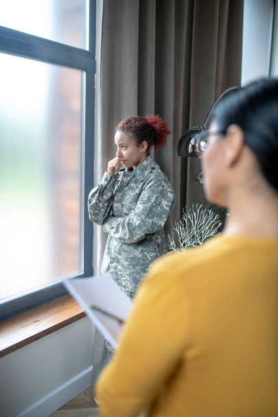 Servicewoman standing near window while visiting psychoanalyst - 写真・画像