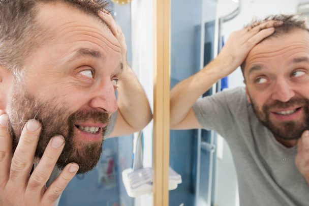 Happy adult man looking at hair in mirror - Zdjęcie, obraz