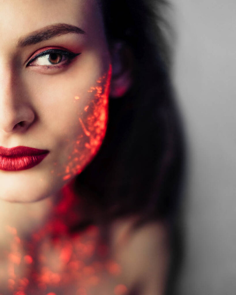 Woman with red glowing uv neon paint on her face and neck. Red lipstick. Brown hair. Fashion portrait - Photo, image