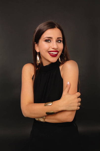 Smiling young woman standing with her arms crossed and looking at camera. She is standing against dark background - Foto, afbeelding