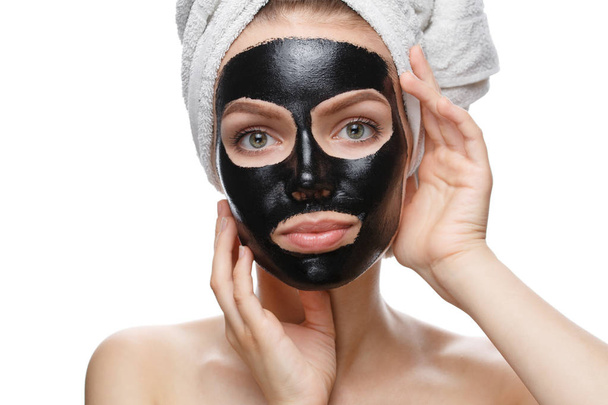 κορίτσι με μαύρη καλλυντική μάσκα στο πρόσωπο και το κεφάλι τυλιγμένο σε πετσέτα - Φωτογραφία, εικόνα