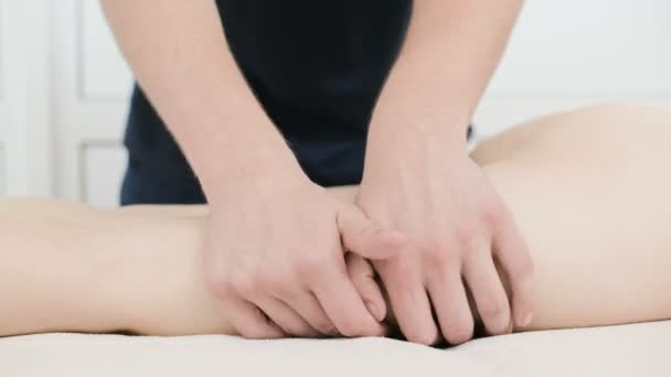 Yakın çekim bir erkek fizyoterapist pamuk bir delikanlı yanında profesyonel bir spa salonunda genç bir kadının kalça ve kalça ısınmak için hafif bir masaj yapıyor. 4k masaj vücut bakım konsepti - Video, Çekim