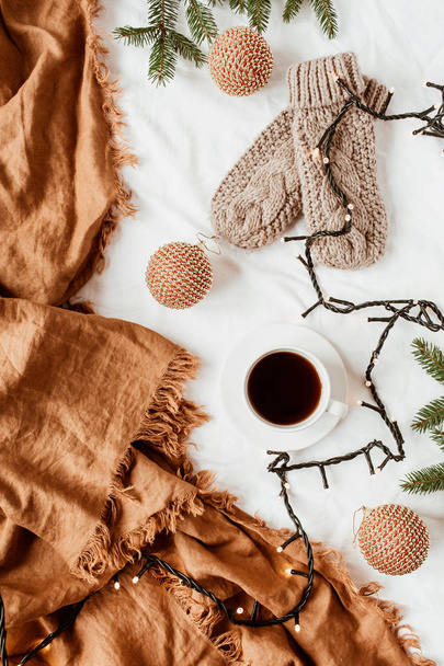 Christmas / New Year composition. Knitted mittens, coffee cup, garland, fir branches, Christmas baubles, ginger plaid. Flat lay, top view decorated holiday background. - Foto, Imagen