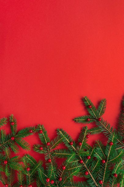 Kerstmis / Nieuwjaar vakantie compositie. Veenboomtakken met bessen op rode achtergrond. Platte lay, bovenaanzicht feestelijk concept. - Foto, afbeelding