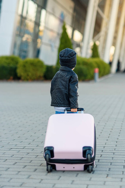 Cute little traveler girl pulls pink suitcase towards the airport. - Photo, Image