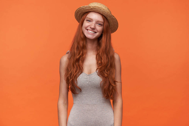 Ritratto orizzontale di piacevole aspetto felice giovane femmina con capelli ondulati volatili isolati su sfondo arancione, indossando abiti casual e cappello di paglia, concetto di emozioni positive
 - Foto, immagini