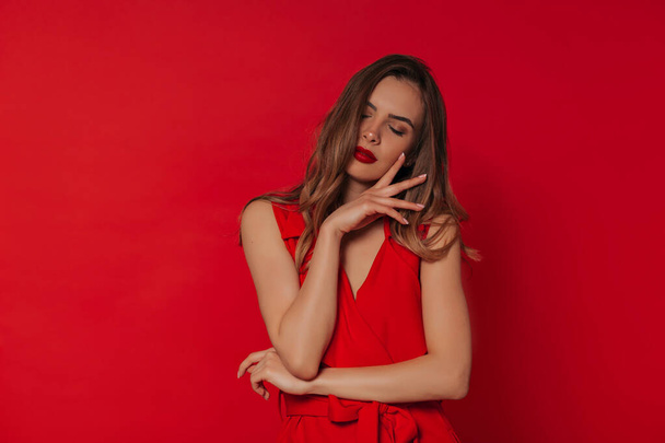 Studio shot Ευρωπαϊκή γυναίκα με κόκκινα χείλη φορώντας κόκκινο φόρεμα που ποζάρει πάνω από το κόκκινο φόντο. - Φωτογραφία, εικόνα