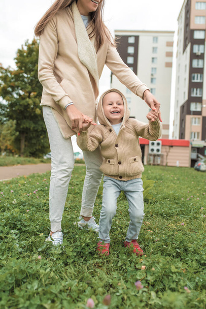 Woman mom plays with little boy son 4-5 years old, in autumn in city, background of building, casual clothes. Having fun playing laughing rejoicing, positive emotions. Beige sweater with a hood. - Fotoğraf, Görsel
