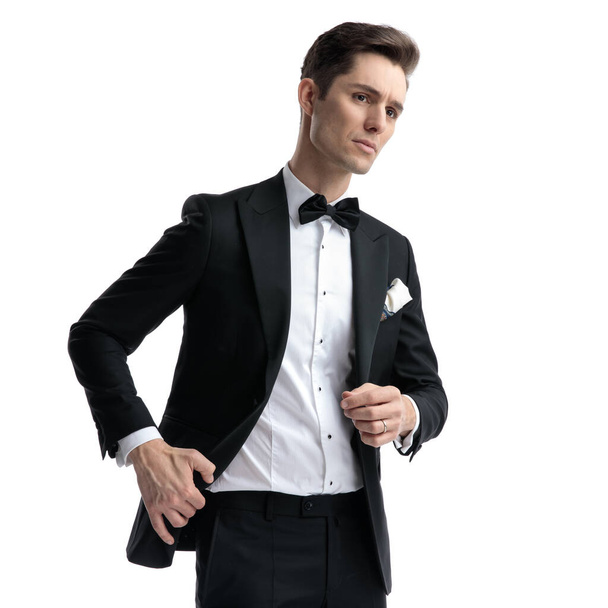 young elegant man looking to side and pulling coat - Zdjęcie, obraz
