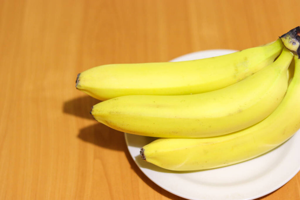Bando de bananas em uma placa branca em uma mesa de madeira com espaço de cópia à esquerda
 - Foto, Imagem