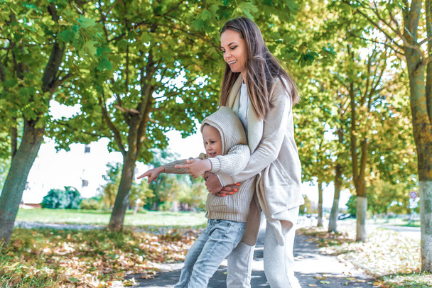 Happy family, young mother woman little boy son 4-5 years old. They play in autumn park. Happy have fun and enjoy weekend. Emotions positive and good mood. Casual wear sweater with hood. - Fotó, kép