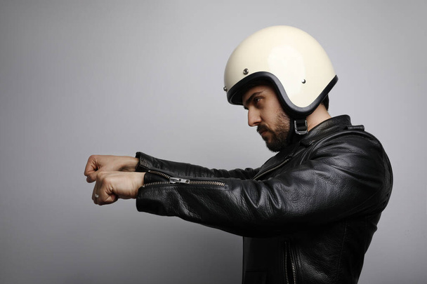 Young biker man in a leather jacket pretending to ride a motorcycle isolated on a white background. Horizontal. - Фото, изображение