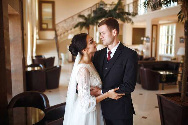 Young wedding couple enjoying romantic moments. Very beautiful wedding of amazing couple. A stylish bridegroom in a black suit gently embraces a beautiful bride in a white dress. Together. Love. - Photo, Image
