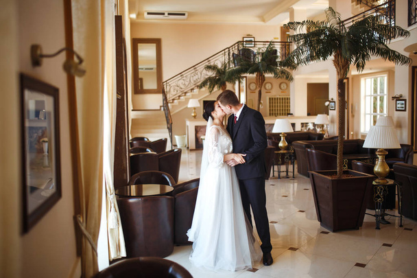 Young wedding couple enjoying romantic moments. Very beautiful wedding of amazing couple. A stylish bridegroom in a black suit gently embraces a beautiful bride in a white dress. Together. Love. - Photo, Image