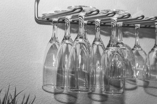 Черно-белое фото группы прозрачных бокалов с красивыми отражениями, висящими на серой металлической полке
 - Фото, изображение