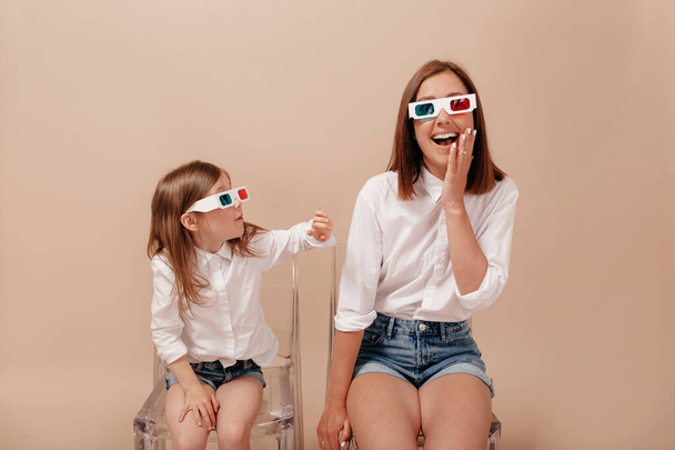 Incredible mother with little cute daughter on chairs. Watching 3D movie in glasses together, expressing positivity - Photo, Image