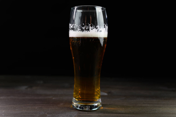 Photo of beer in a glass. Thick foam and a nice color drink on a black background. - Fotó, kép
