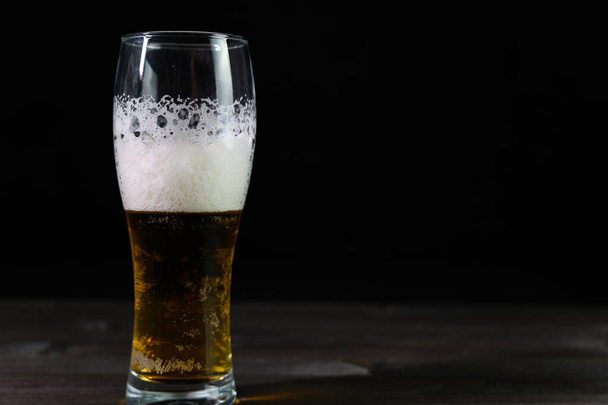 Photo of beer in a glass. Thick foam and a nice color drink on a black background. - Foto, Imagem