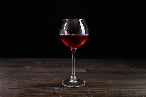 Photo of red wine in a glass on a wooden table. Nice color drink on a black background. - Foto, Imagen