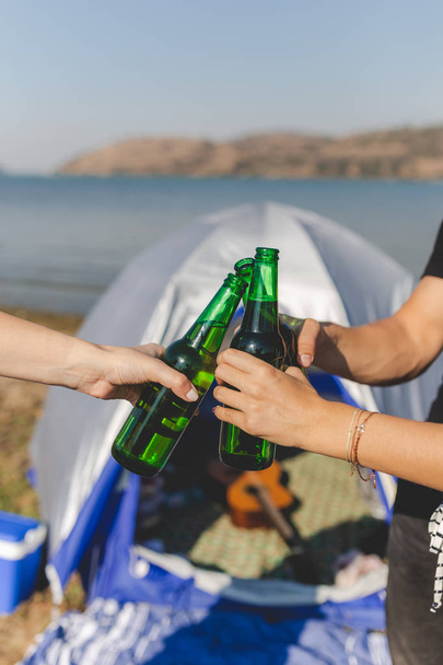Close up of hands holding beer and cheering against camping tent at the beach. - Foto, Imagem