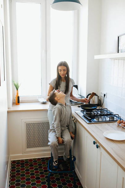 Cute little boy and his mom smiling and cooking in kitchen at home - Foto, imagen