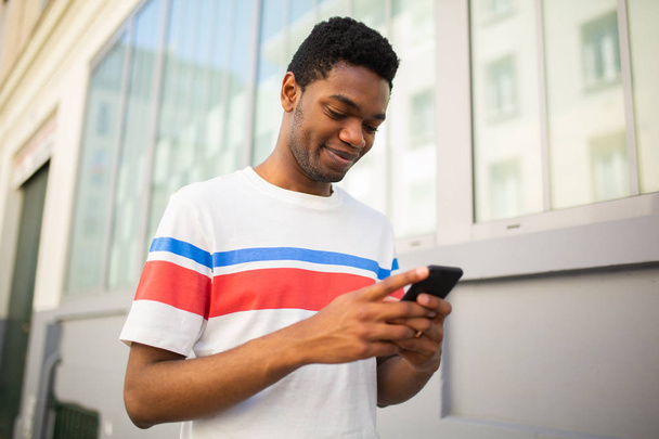 Close up retrato de jovem afro-americano caminhando na cidade e olhando para o celular
  - Foto, Imagem