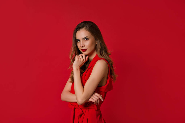 Señora bonita confiada con vestido rojo con labios rojos posando a la cámara sobre fondo rojo
 - Foto, imagen