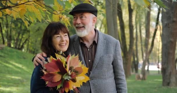 高齢者のカップルは、木々の間の居心地の良い公園で幸せを笑い、抱きしめ、晴れた秋の日を楽しむ-スローモーション。引退後の現役現代生活。幸せと笑顔. - 映像、動画