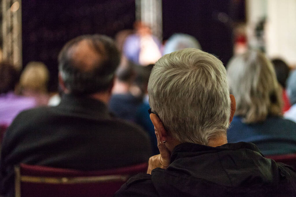 Kısa saçlı kadın da seyircilerin bir parçası. Halka açık bir konferansı dinliyor. - Fotoğraf, Görsel