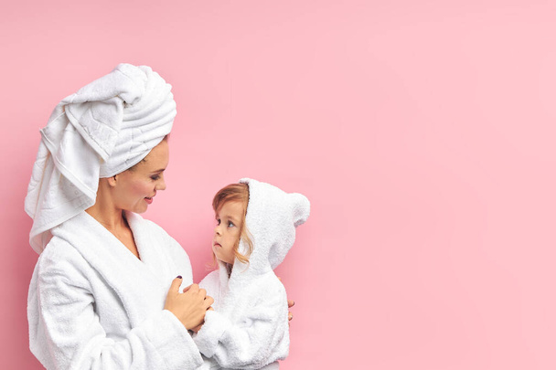Young mother with cute daughter after bathing in white towels - Foto, afbeelding