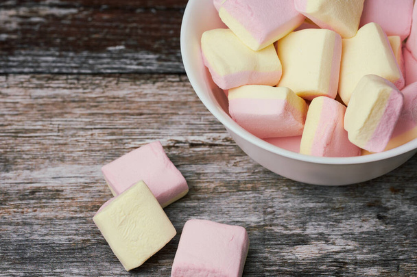 rózsaszín és sárga mályvacukor egy fehér tál fa felületen, összpontosít az édességek a tálban - Fotó, kép