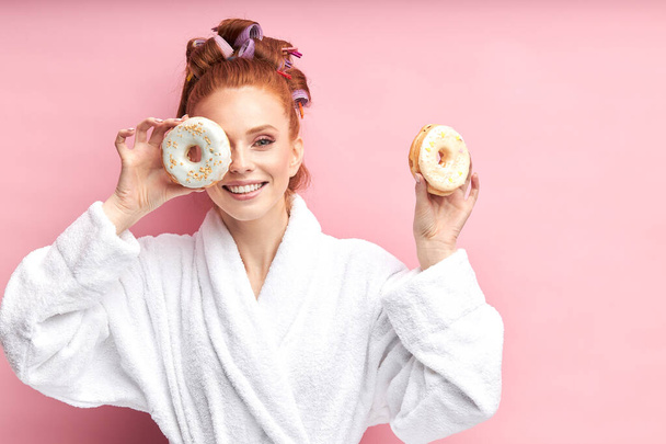lovely girl in home clothes posing with donuts on pink background - Фото, изображение