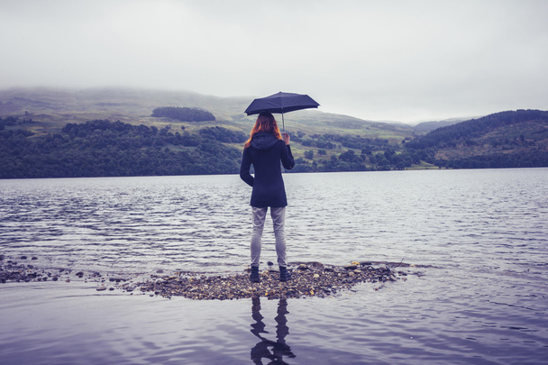 Young woman with an umbrella standing in lake - Фото, изображение