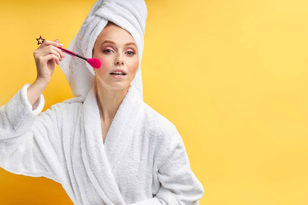 Gorgeous lady wearing bathrobe doing make-up with tassels - Foto, afbeelding