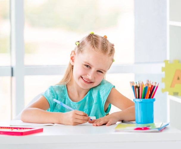 Cute kid girl sitting at the desk, coloring with pencils - Photo, image