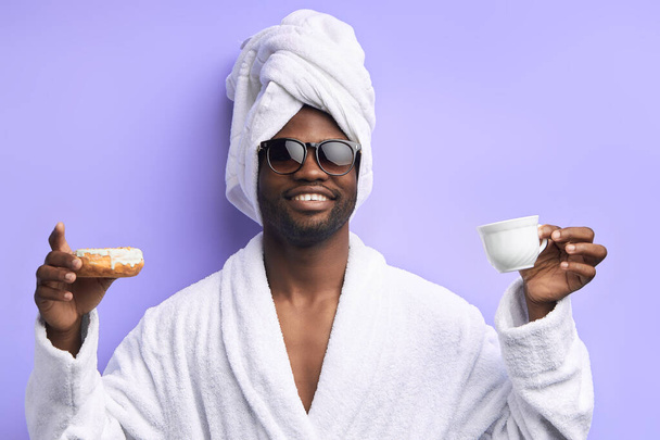 Excited young african man holding glazed donut and cup of tea or coffee - Foto, Imagem