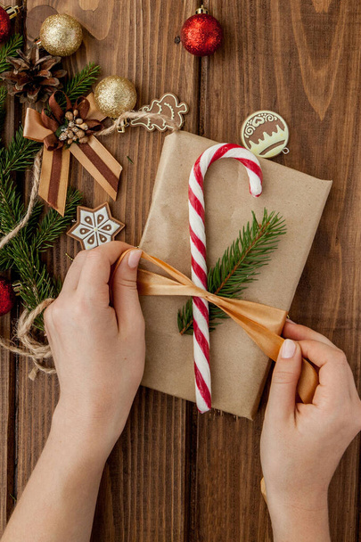Woman s hands wrapping Christmas gift, close up. Unprepared christmas presents on wooden background with decor elements and items, top view. Christmas or New year DIY packing Concept. - 写真・画像