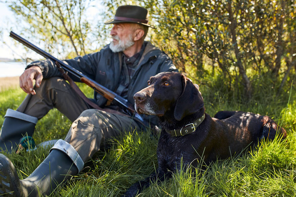 Starší kavkazský lovec sedící se psem na trávě - Fotografie, Obrázek