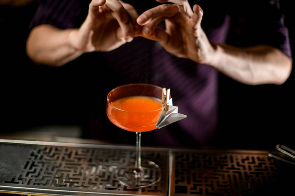 Barman spuiten op de cocktail in het glas versierd met papier vliegtuig in de wasknijper met een sinaasappelschil sap - Foto, afbeelding