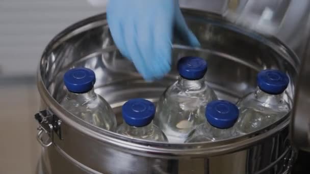Laboratoriummedewerker stopt medicijnflesjes in sterilisatie container. - Video