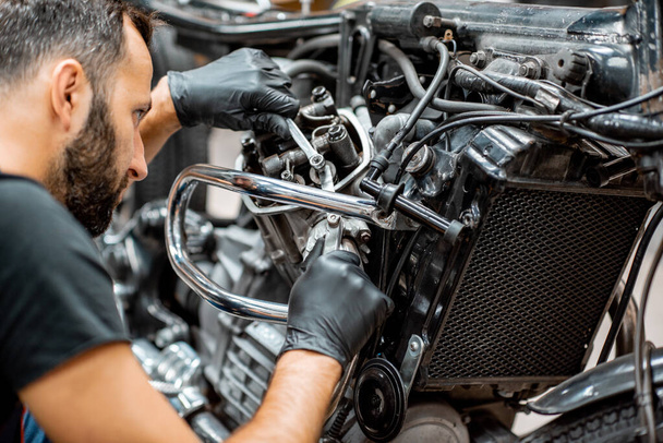 Trabajador reparando motor de motocicleta en el taller
 - Foto, Imagen