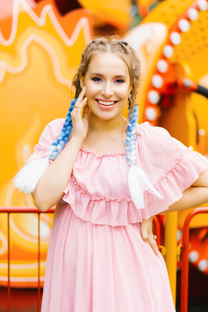 Όμορφη όμορφη κοπέλα με κοτσίδες με μπλε χρώμα μαλλιών με όμορφο φωτεινό make-up χαμογελά στο φόντο των φωτεινών αξιοθέατων - Φωτογραφία, εικόνα