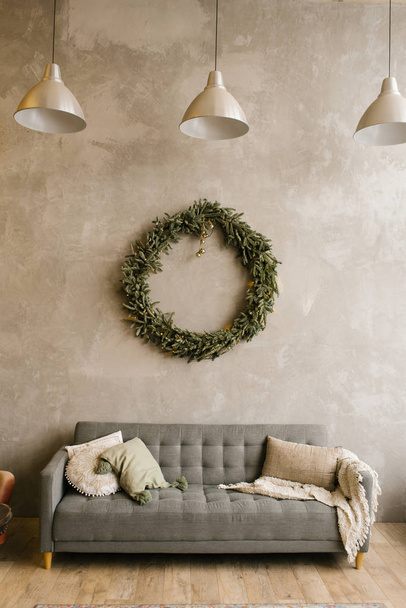 Сірий диван з подушками і різдвяний вінок на стіні у вітальні
 - Фото, зображення