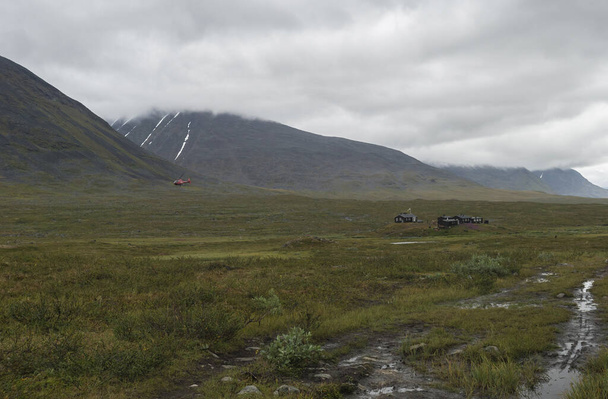 Поставки красного вертолета Туристы в хижине Mountain Lodge Salka STF. Лапландская горная лестница в летний облачный день
. - Фото, изображение