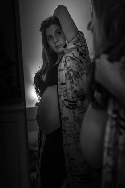 Pregnancy, motherhood, people and expectation concept - happy pregnant woman looking to mirror at home. Black and white photography. - 写真・画像