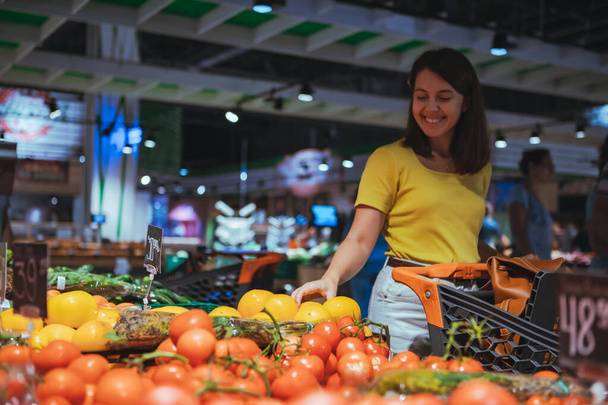 woman choosing yellow tomatoes from store shelf grocery shopping - Photo, Image