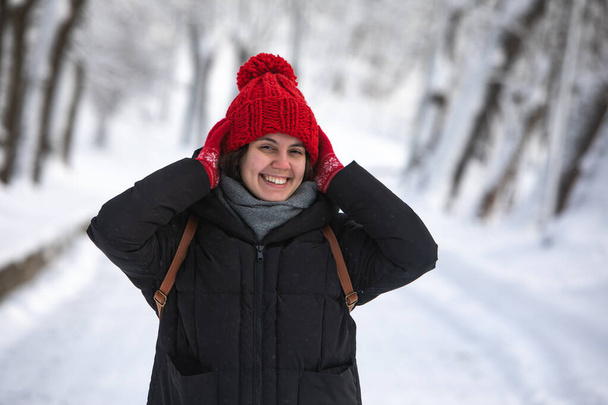 молода досить усміхнена жінка в зимовому пальто з червоним капелюхом в міському лісовому парку
 - Фото, зображення